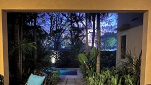 A patio area with a stone pathway leading to a pool, surrounded by lush greenery and outdoor furniture. - Tropical Retreat - 3 BDR/2 Bath condo, 2 min. walk to the Pacific Ocean. (Tamarindo)