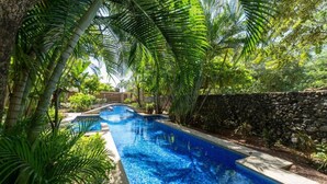 A swimming pool surrounded by lush greenery and a stone wall. - Tropical Retreat - 3 BDR/2 Bath condo, 2 min. walk to the Pacific Ocean. (Tamarindo)
