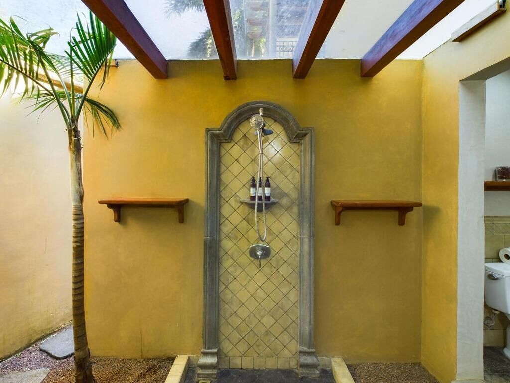 A shower area with a tiled wall, a palm tree, and wooden shelves.