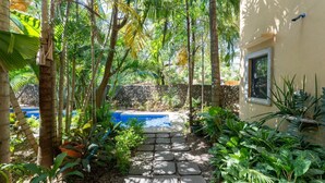 A stone pathway leading to a pool surrounded by lush tropical vegetation and a stone wall. - Tropical Retreat - 3 BDR/2 Bath condo, 2 min. walk to the Pacific Ocean. (Tamarindo)