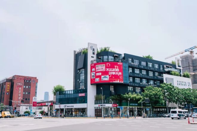 A modern building with a prominent red advertisement on the side, surrounded by other commercial buildings and a busy street with vehicles.