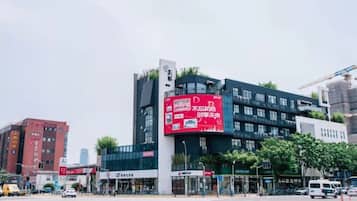 A modern building with a prominent red advertisement on the side, surrounded by other commercial buildings and a busy street with vehicles.