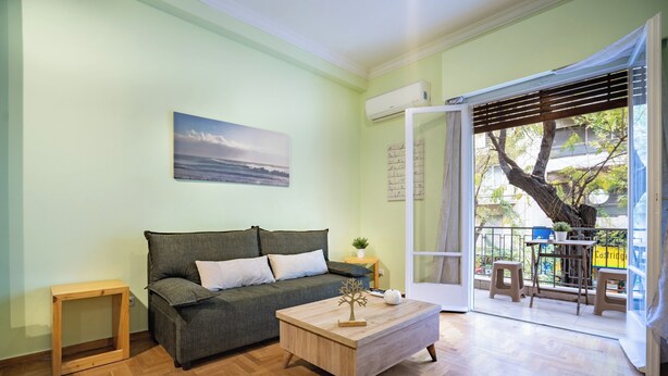 Una sala de estar con sofá, una mesa de centro y vistas a un balcón con mobiliario exterior.