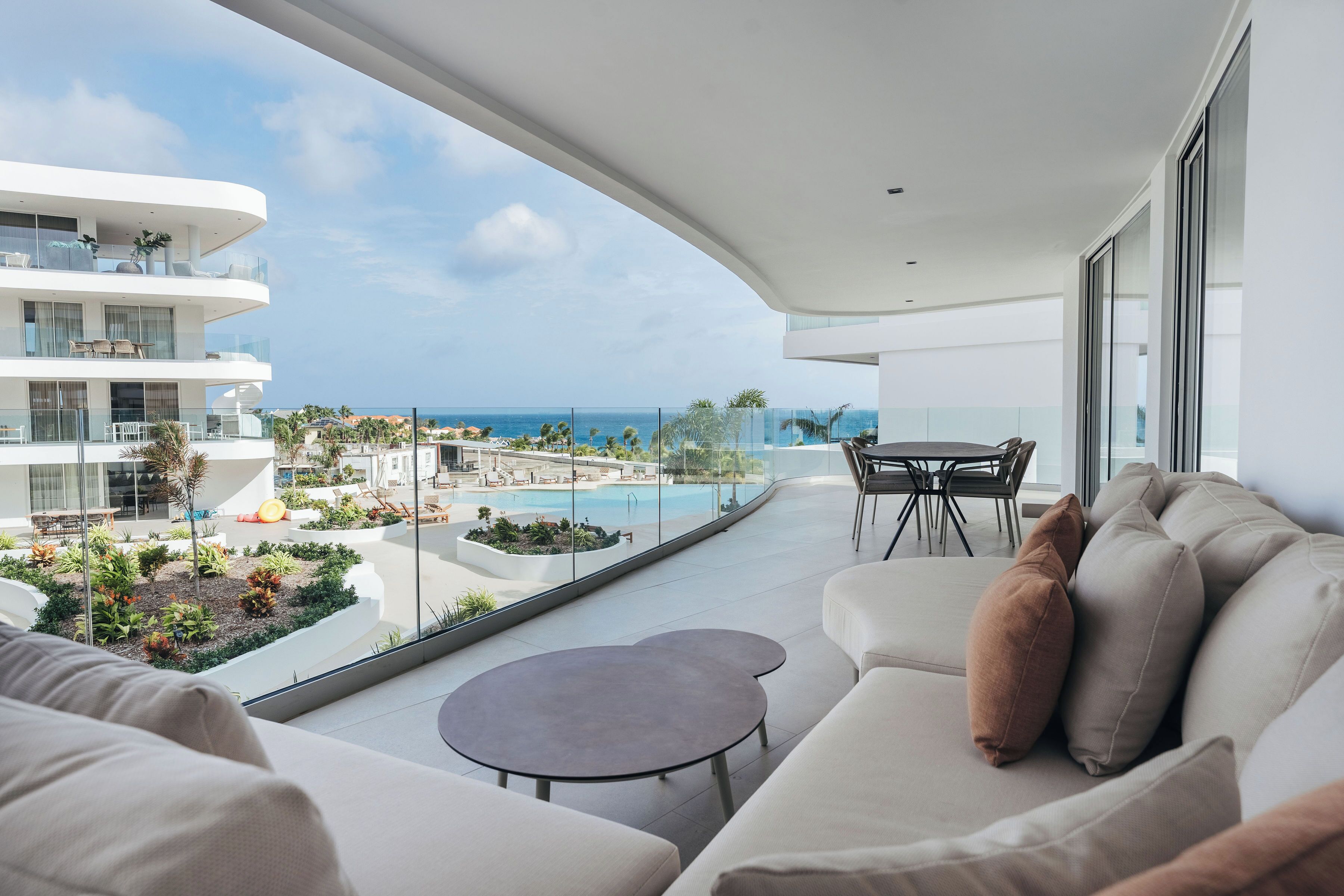 A modern balcony with a view of a pool and ocean, featuring a sofa and a small table.
