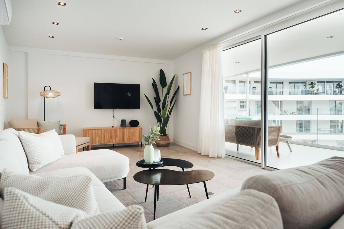 Ein modernes Wohnzimmer mit einer Couch, einem Couchtisch, einem Fernseher und einem großen Fenster.