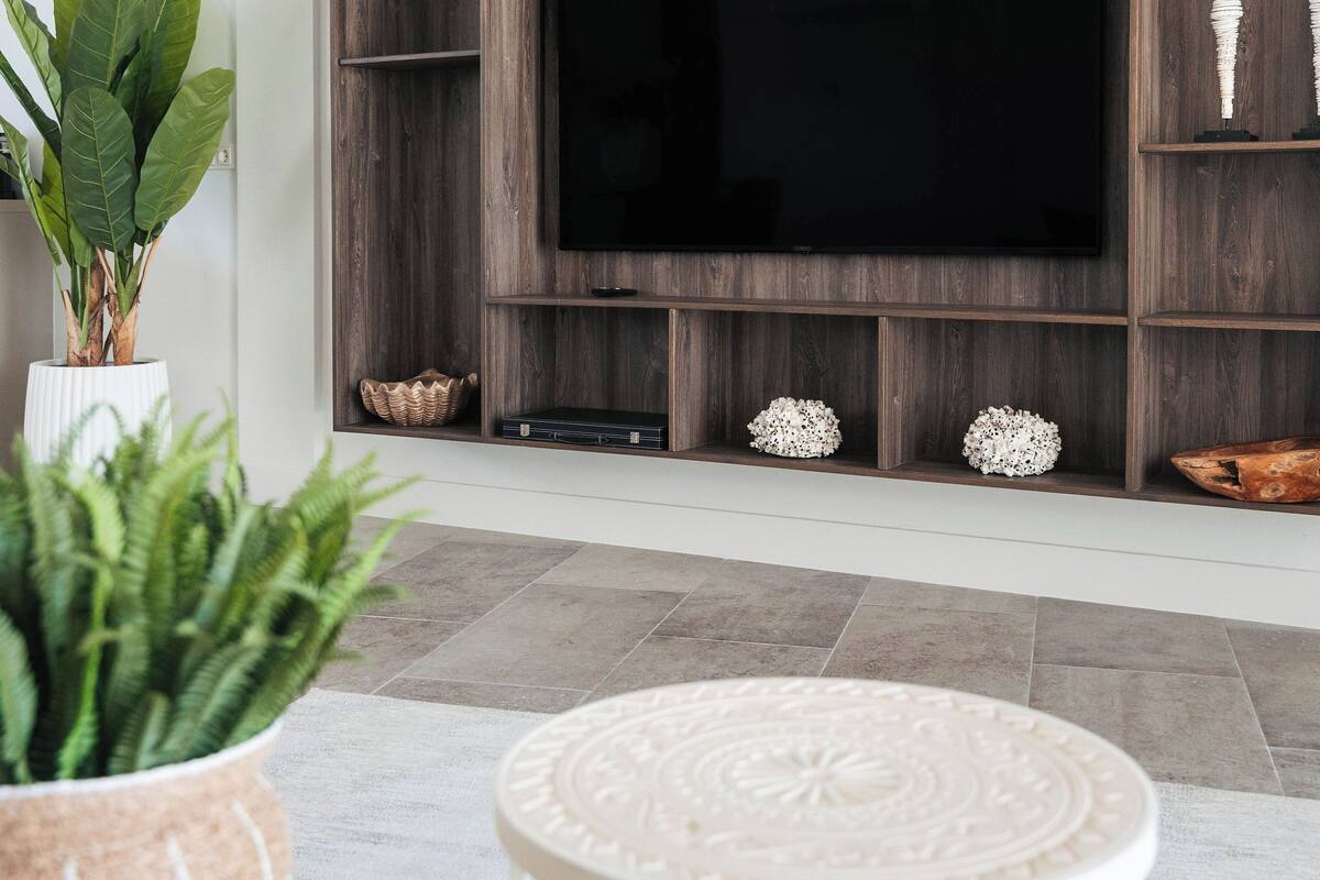 Ein modernes Wohnzimmer mit einem großen Flachbildfernseher, der an einer holzverkleideten Wandkonsole angebracht ist, umgeben von Regalen und Dekoration.
