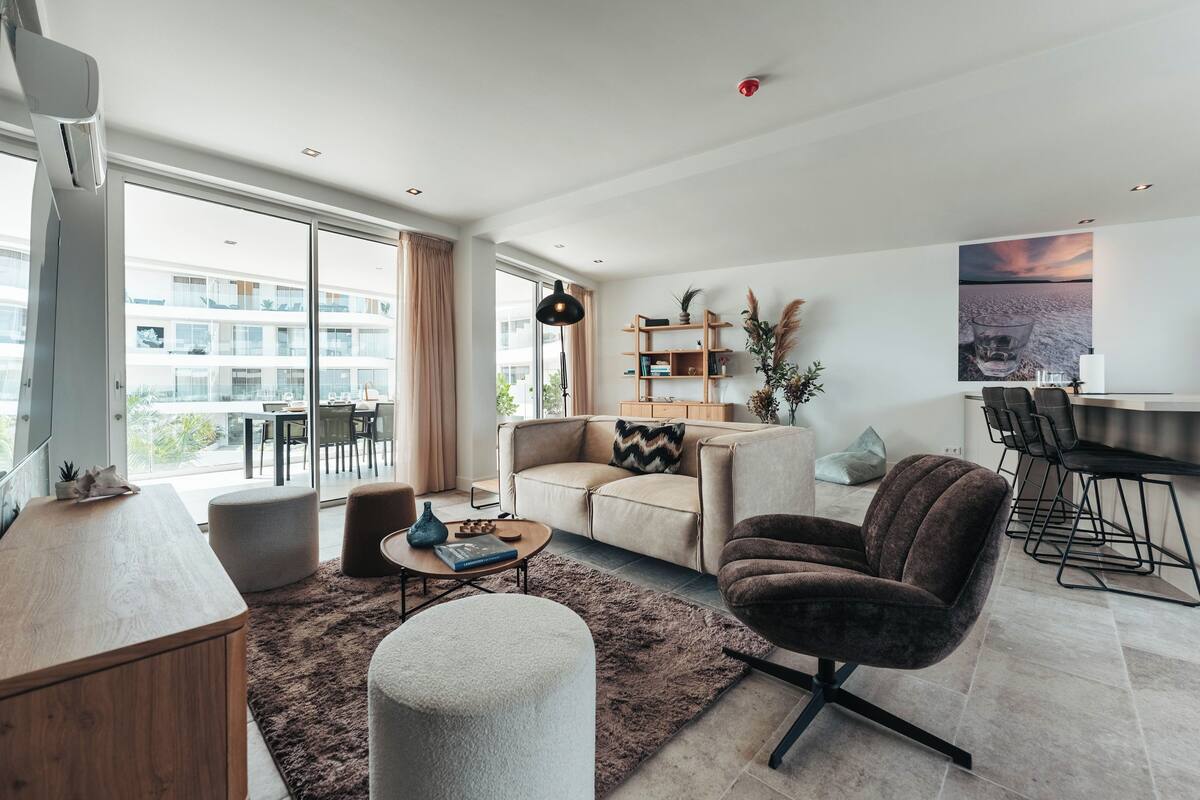 Ein modernes Wohnzimmer mit Sofa, Sessel, Couchtisch und einem Essbereich mit Stühlen und Tisch.