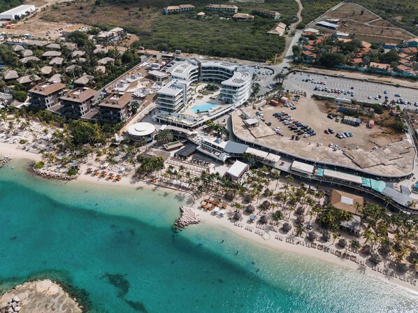 Vue aérienne d’une station balnéaire comprenant un bâtiment central, plusieurs villas situées en bord de mer et un espace de stationnement.