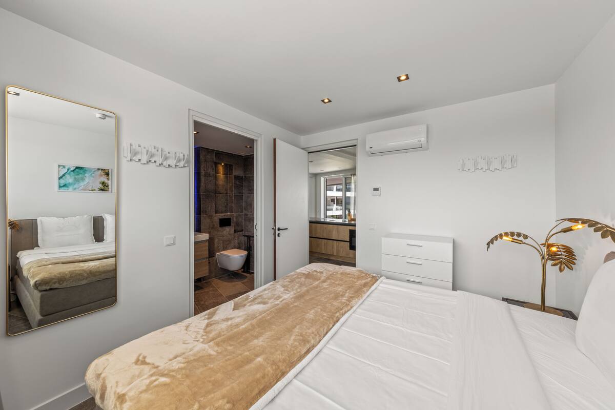 Ein modernes Schlafzimmer mit einem großen Bett, einem Nachttisch, einem Spiegel und einer Wand-Klimaanlage.