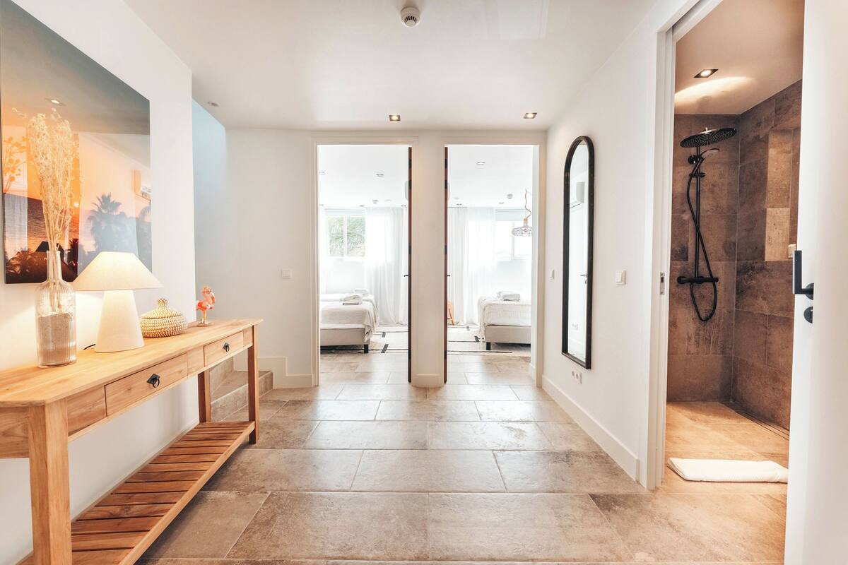 Ein modernes Badezimmer mit Dusche, Waschtisch und Spiegel, mit Blick ins Schlafzimmer.
