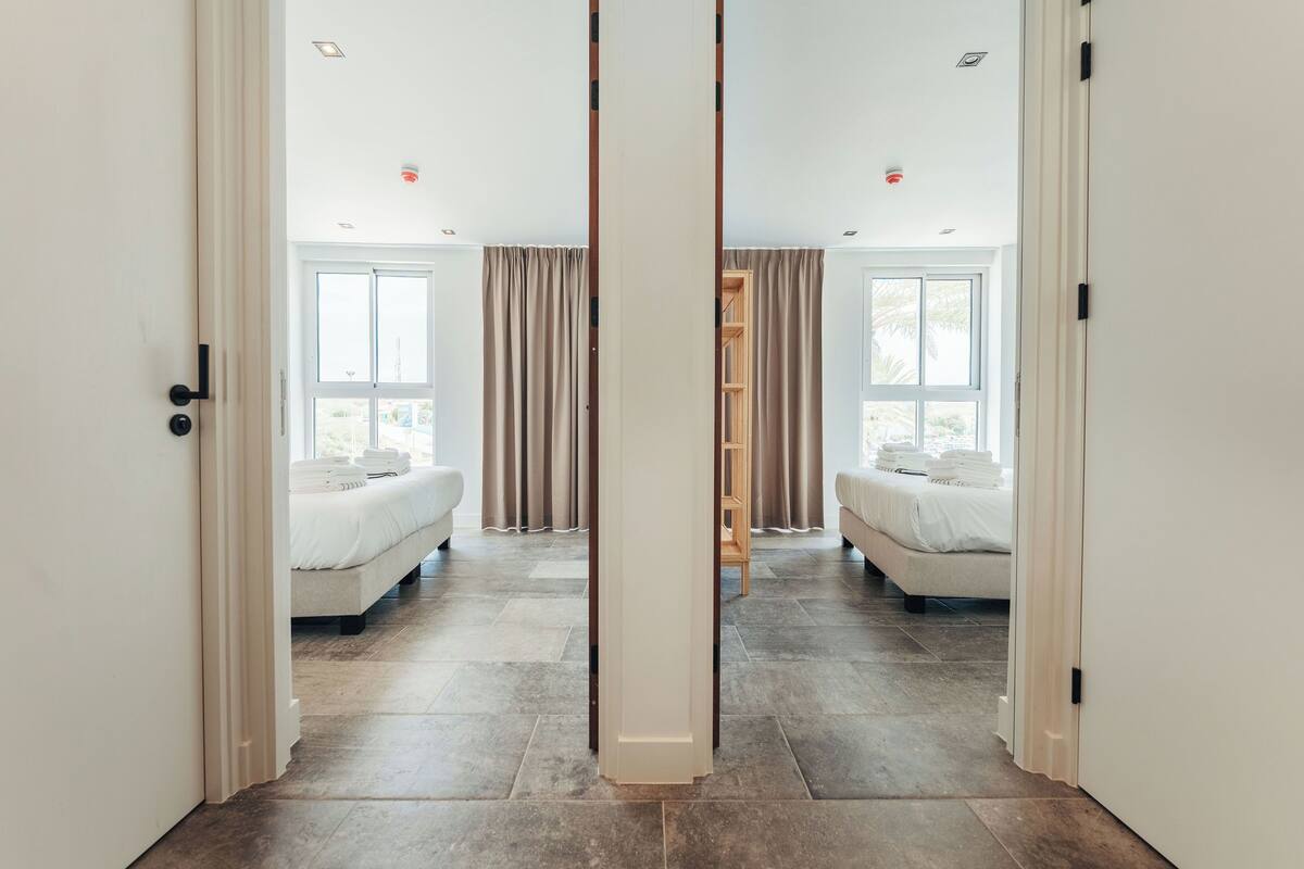 Ein Hotelzimmer mit großem Spiegel, zwei Betten, einem Kleiderschrank und Blick ins Freie.