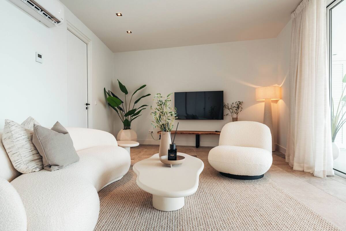 Ein modernes Wohnzimmer mit Sofa, Sessel und Couchtisch, einem Flachbildfernseher und einer Lampe.