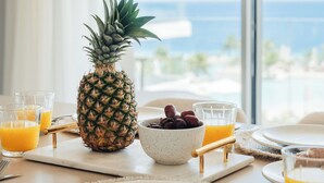 A breakfast setting with a pineapple, a bowl of grapes, and glasses of orange juice on a table with a view of the ocean. - ONE Mambo by Bocobay (Willemstad)