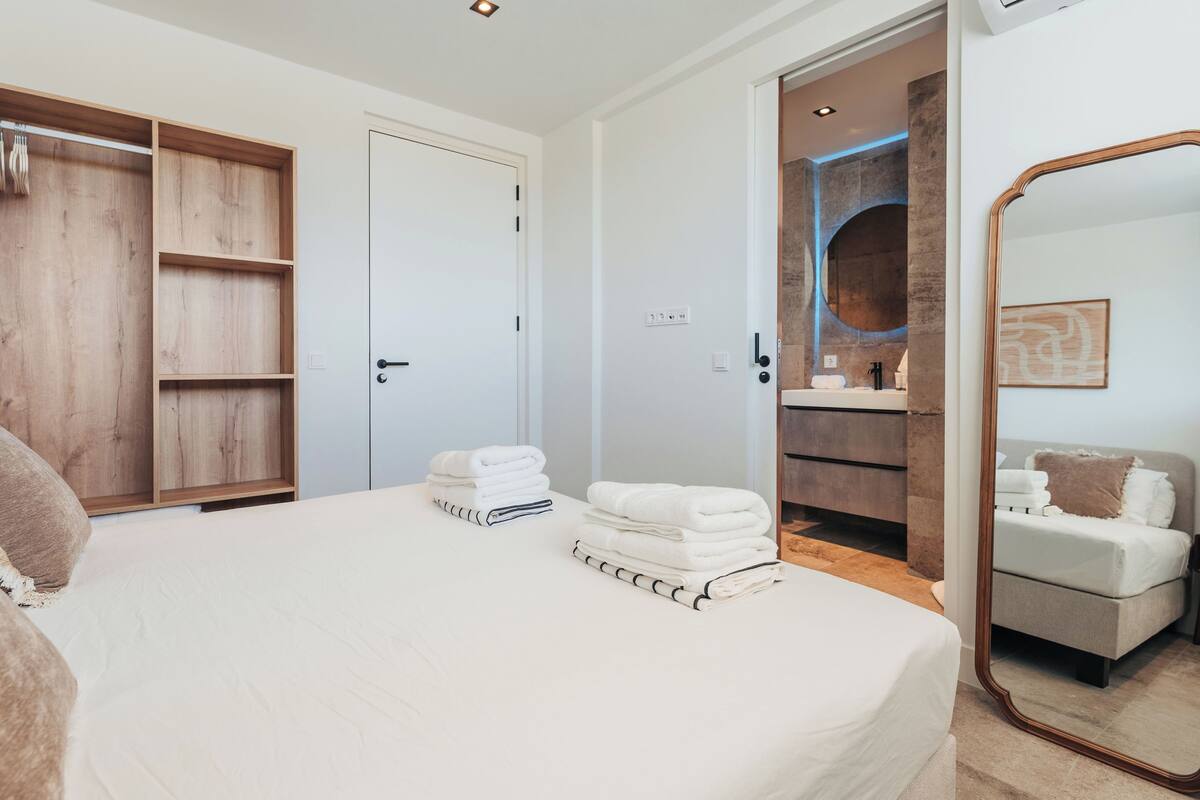 Ein Schlafzimmer mit einem großen Bett, einem Holzschrank, einem Badezimmer mit Spiegel und einer kleinen Sitzecke.