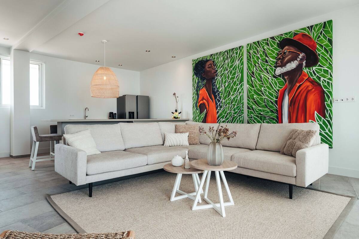 Ein modernes Wohnzimmer mit einem beigefarbenen Ecksofa, einem runden Couchtisch und einem großen abstrakten Gemälde an der Wand.