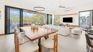 A spacious living room with a large wooden dining table, white sofas, and a flat-screen TV mounted on the wall. - 5BR Luxury Villa, Large Pool, 3-Min Walk to Beach, Concierge (Cabo Velas, Santa Cruz)