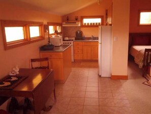 Kitchen area with dining table, refrigerator, stove, and sink, adjacent to a cozy bedroom with a bed and window.