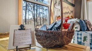 Mandje van riet met een handgeschreven briefje op een standaard, een raam met uitzicht op bomen en een geruit sprei.
