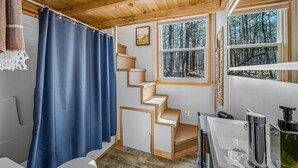 A wooden cabin interior with a staircase, a bathroom, and large windows offering a forest view. - Tiny Cub House | Secluded Tiny House on 1.7 Acres, Mentone (Mentone)