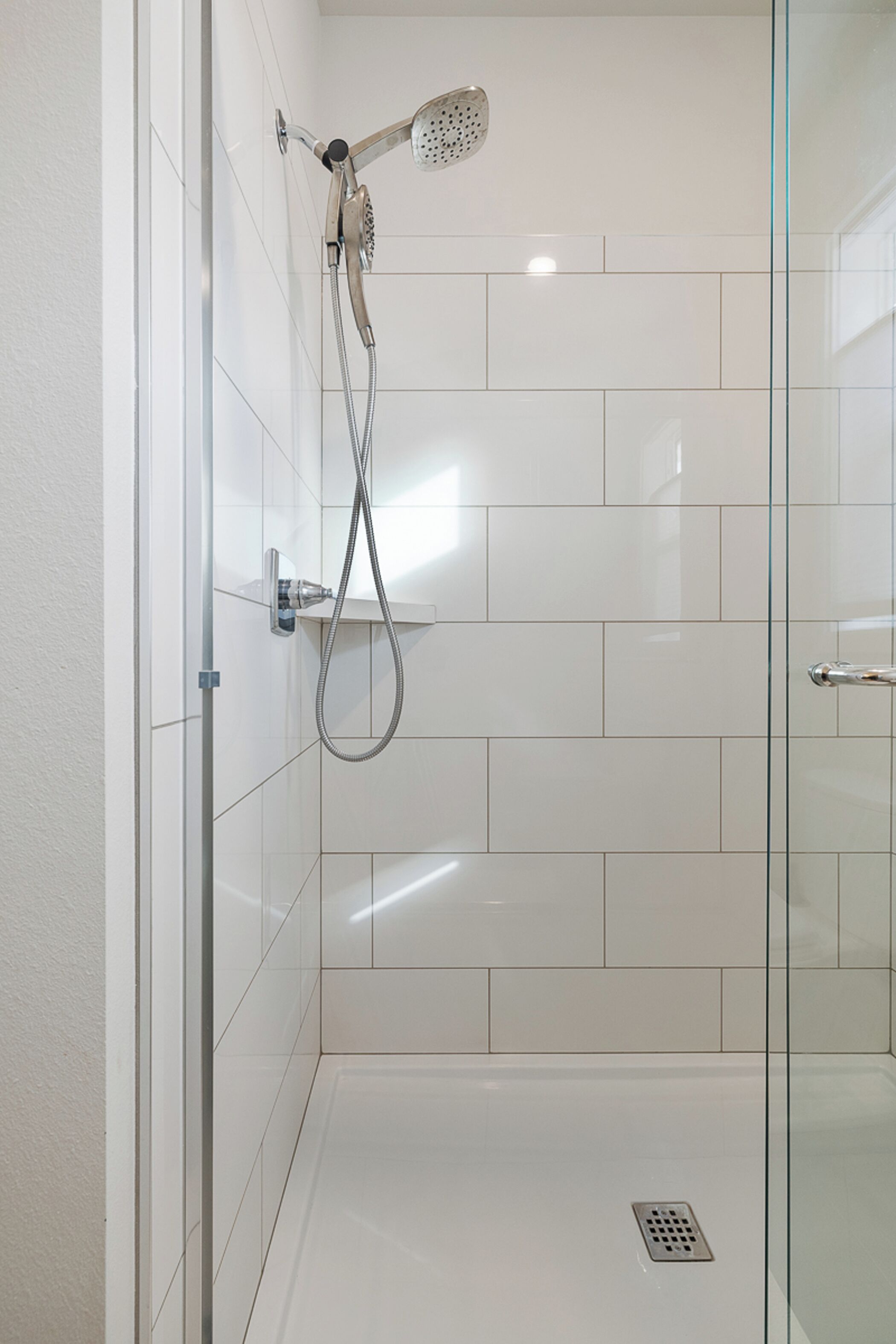 A glass-enclosed shower with a handheld showerhead and a wall-mounted control panel.