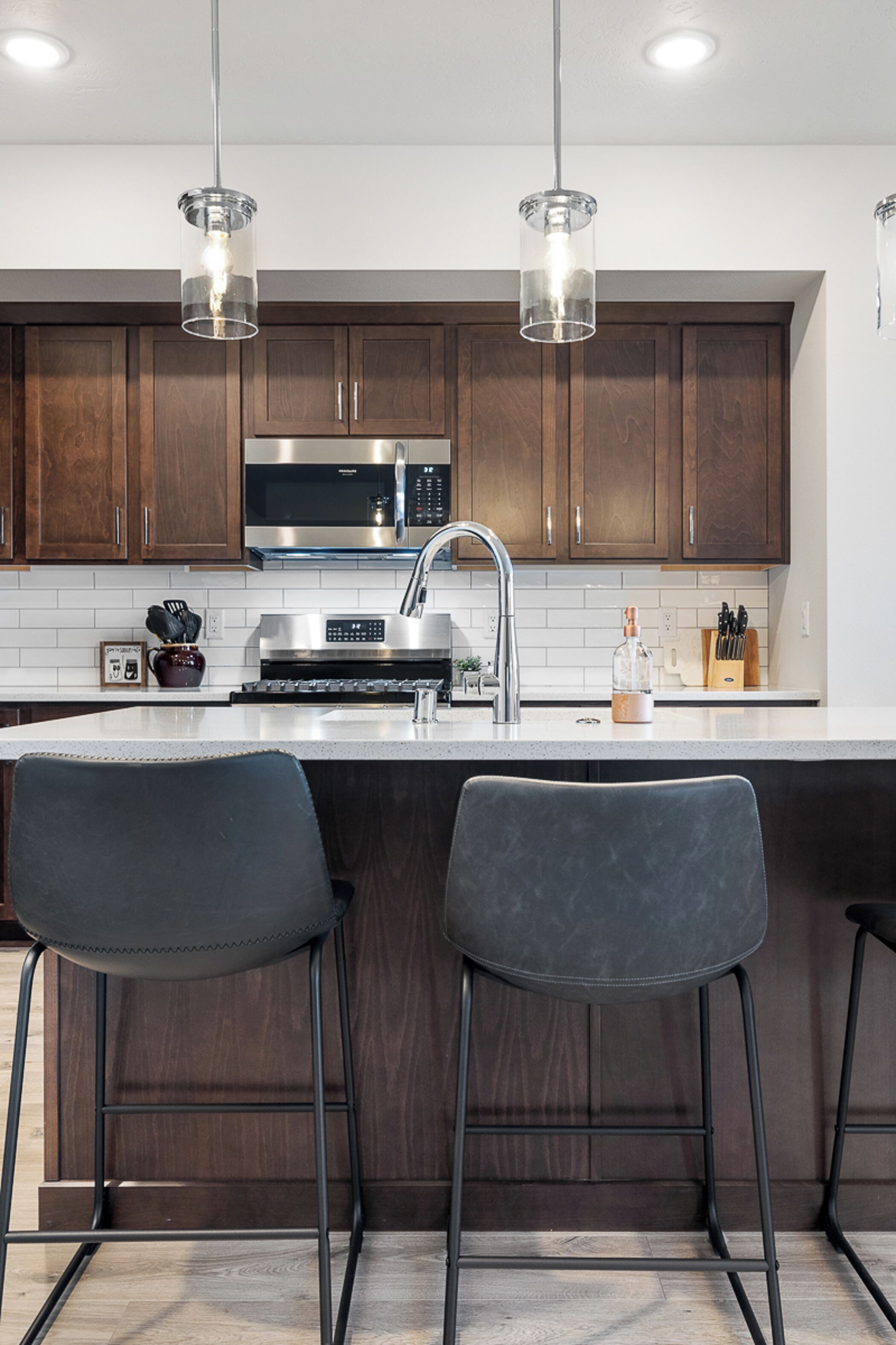 A modern kitchen with dark wooden cabinets, stainless steel appliances, and two bar stools.
