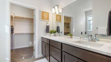 A modern bathroom with a large mirror, two sinks, and a walk-in closet.