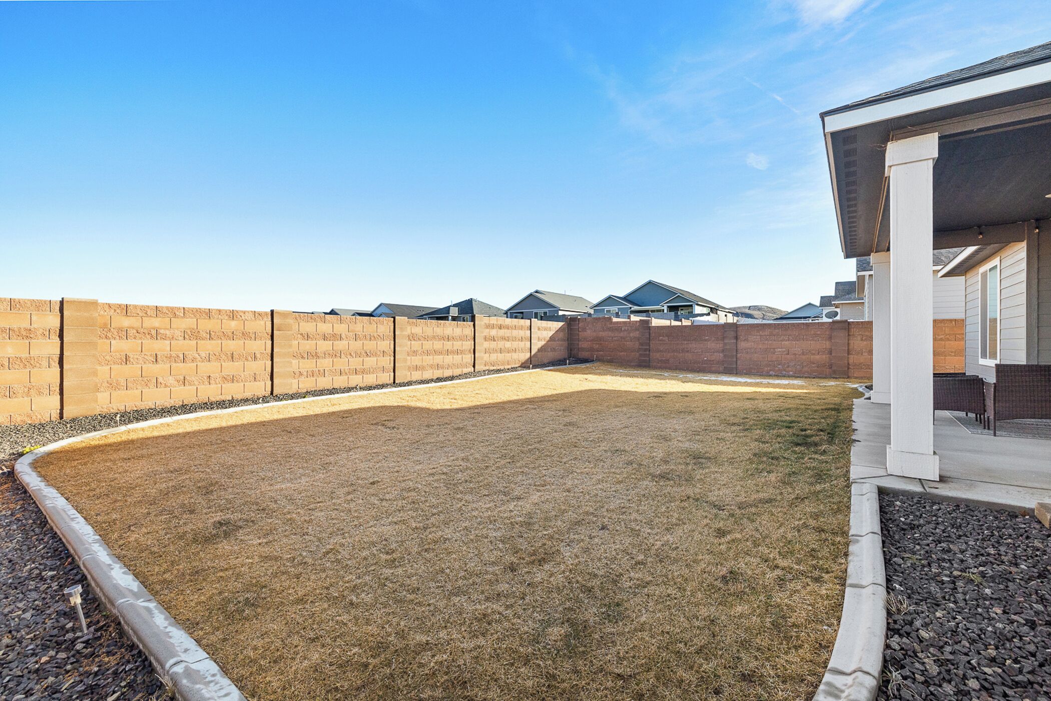 A backyard with a brick wall, a grassy area, and a patio with outdoor furniture.