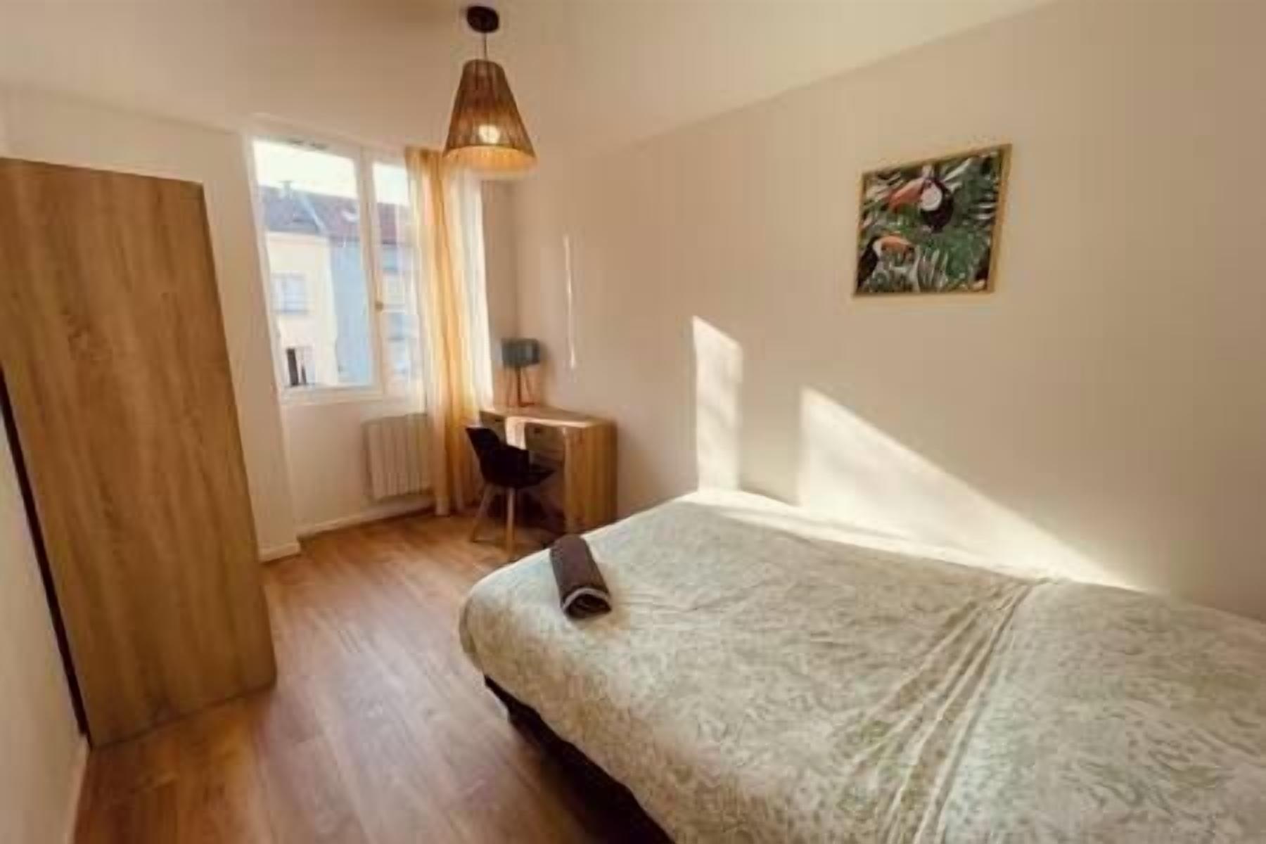 A bedroom with a bed, a desk, a chair, a radiator, and a window.