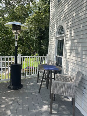 Un espacio al aire libre cubierto con una mesa, sillas, un cubo de basura y una valla blanca.