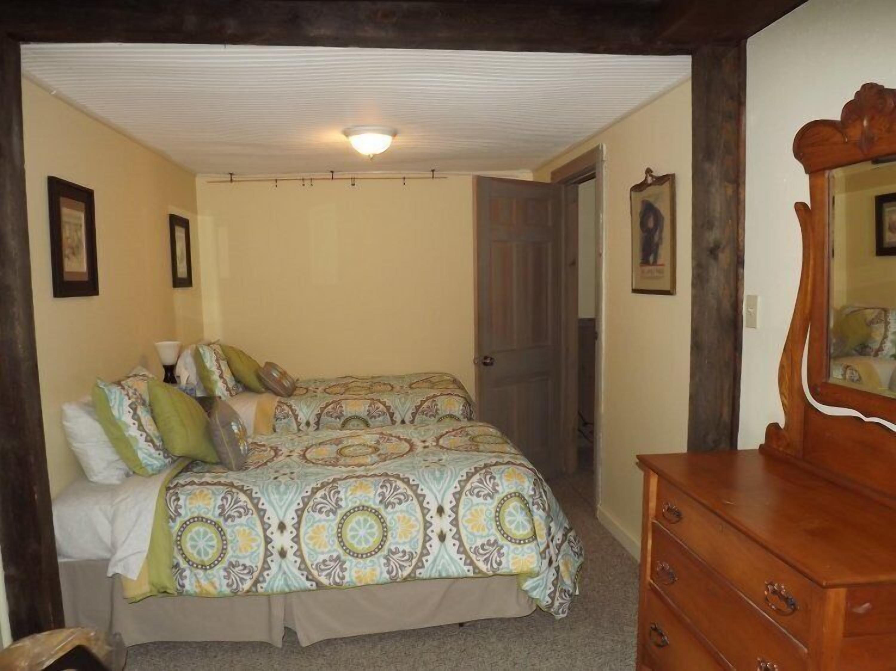 A bedroom with two beds, a wooden dresser, and a ceiling light.