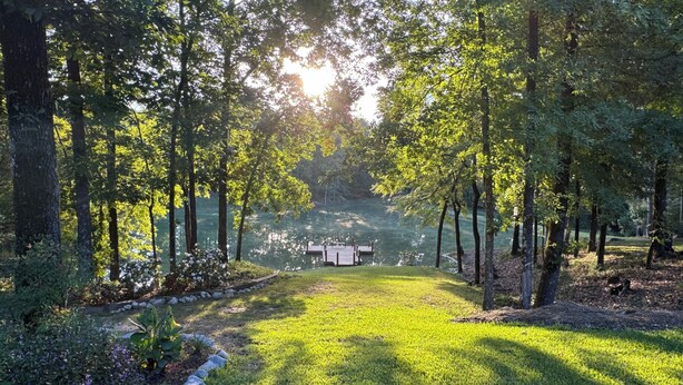 A serene park with a grassy lawn, a wooden dock, and a lake surrounded by trees. - Charming 2-bedroom cabin with AC just 3 miles from Sardis lake. (Sardis)