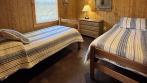 A room with two beds, wooden walls, a ceiling fan, a window with blinds, and a wall-mounted lamp. - Charming 2-bedroom cabin with AC just 3 miles from Sardis lake. (Sardis)
