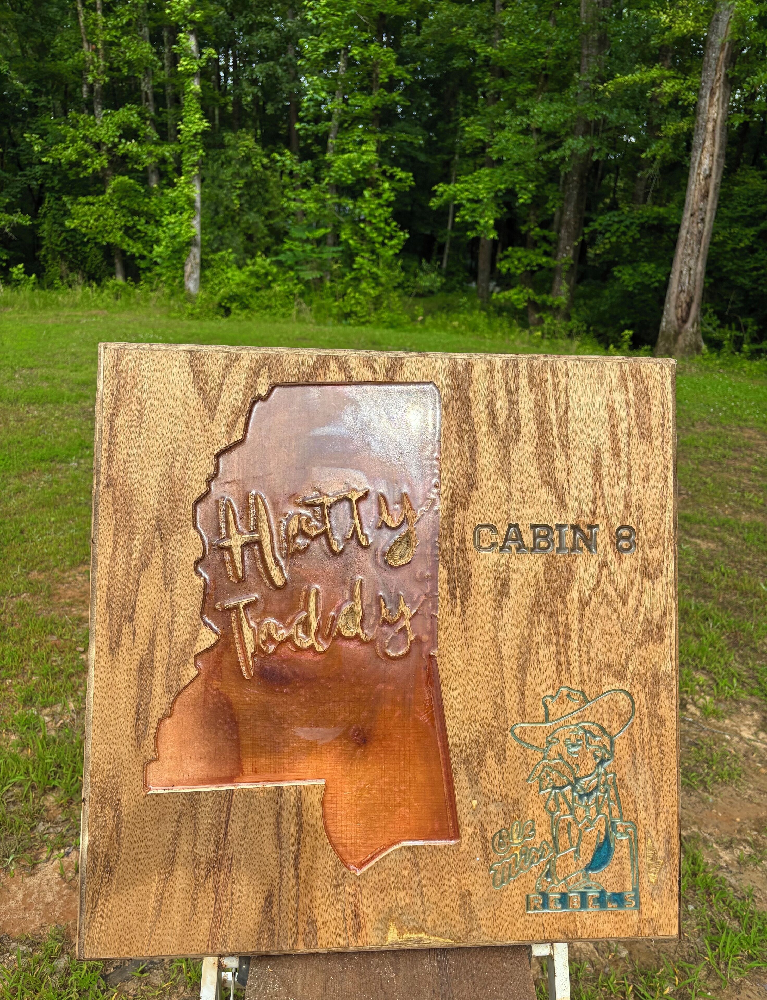 A wooden sign with a map outline and text reading "Holly Taddy" and "CABIN 8".