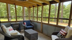 A covered outdoor seating area with wicker furniture, a table, and a view of the forest. - Charming 2-bedroom cabin with AC just 3 miles from Sardis lake. (Sardis)