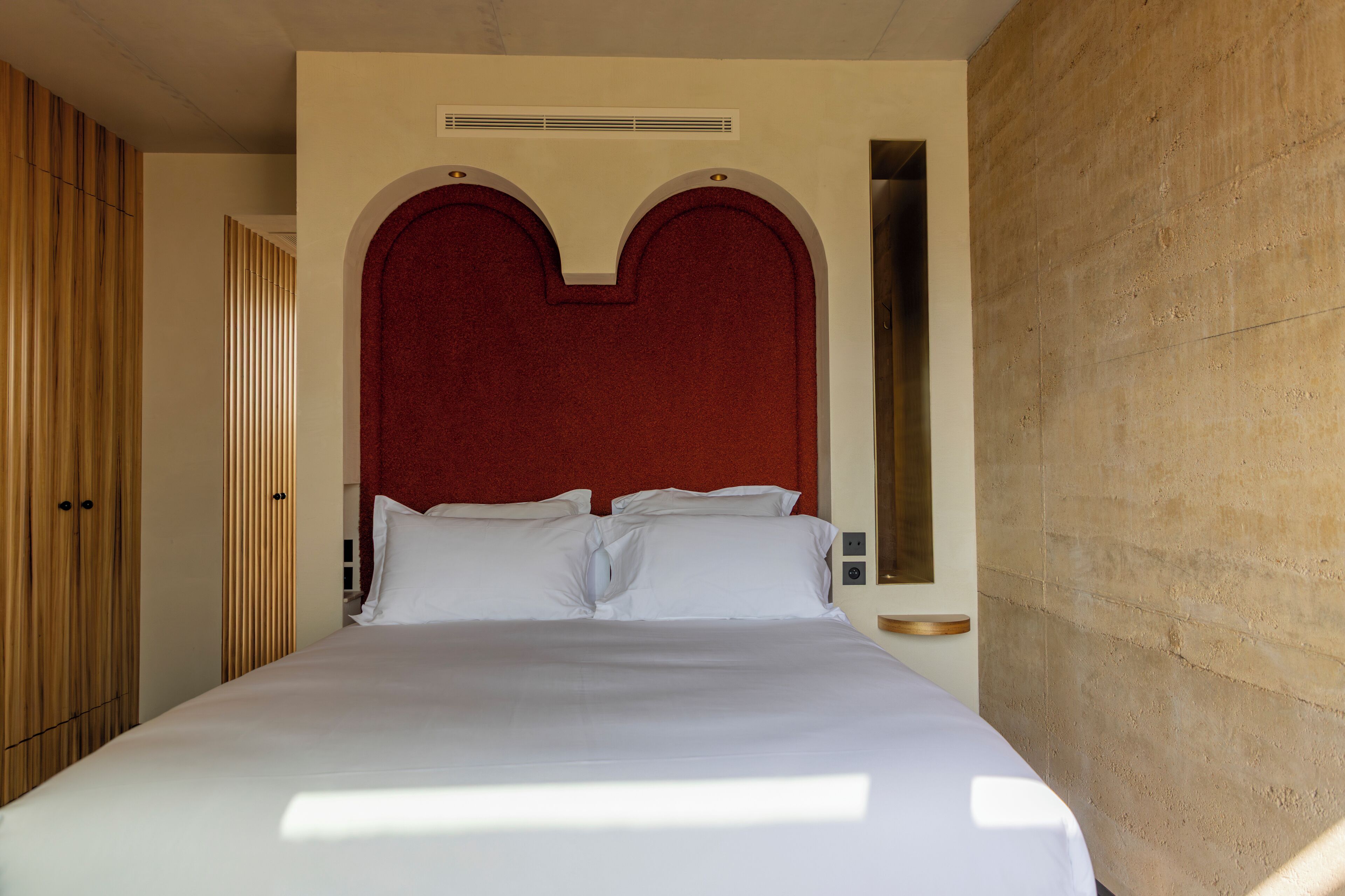 Une chambre d’hôtel avec un grand lit, une armoire en bois et un mur d’accent de couleur rouge.