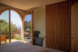 Un dormitorio con una cama grande, un armario de madera y un ventanal corredero que da a un balcón con vistas al mar.