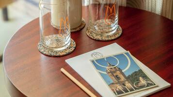 A round wooden table with two clear glass candle holders, a white vase, a wooden stick, and a postcard.
