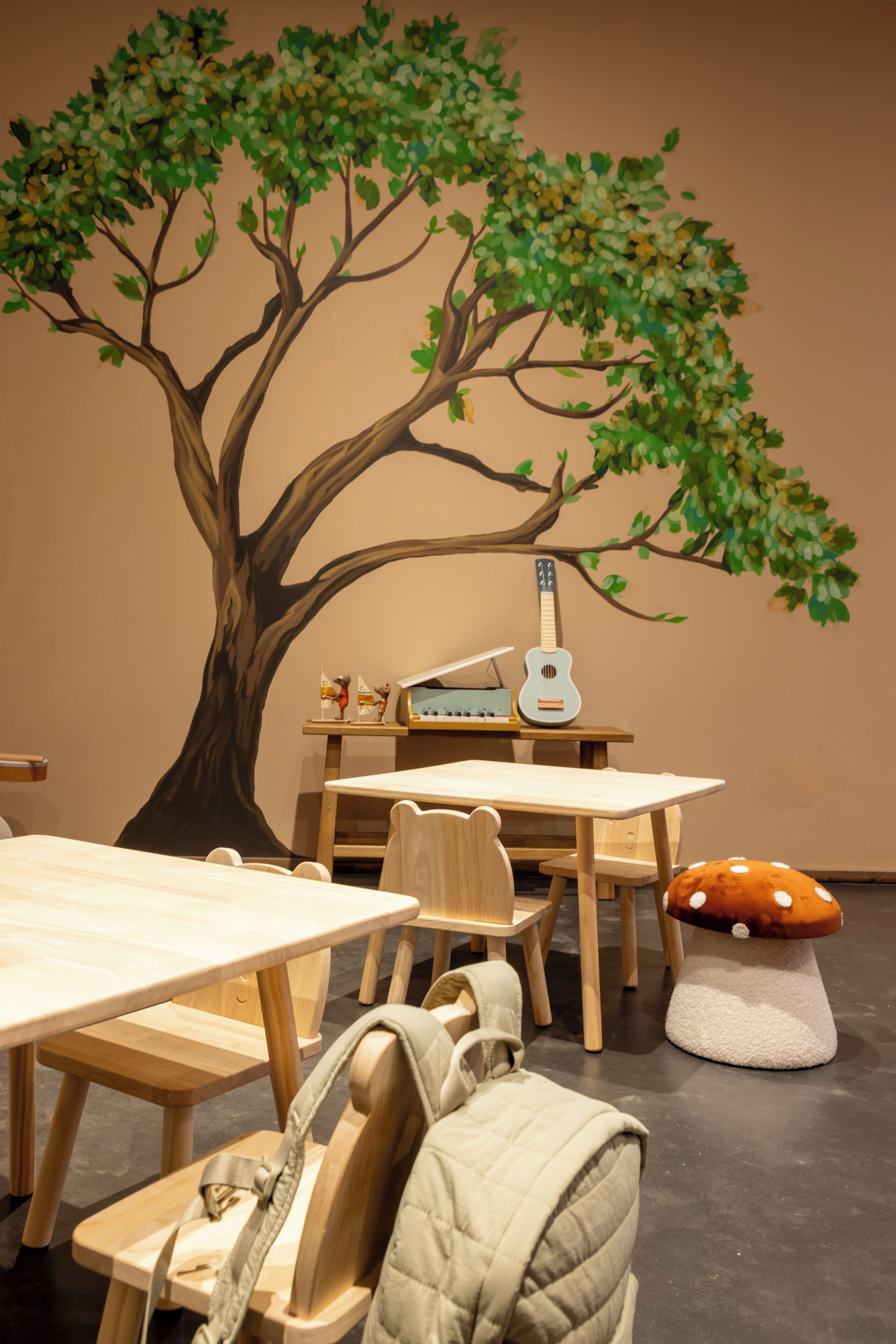 A room with a large tree mural, wooden furniture, a guitar, and a mushroom-shaped cushion.
