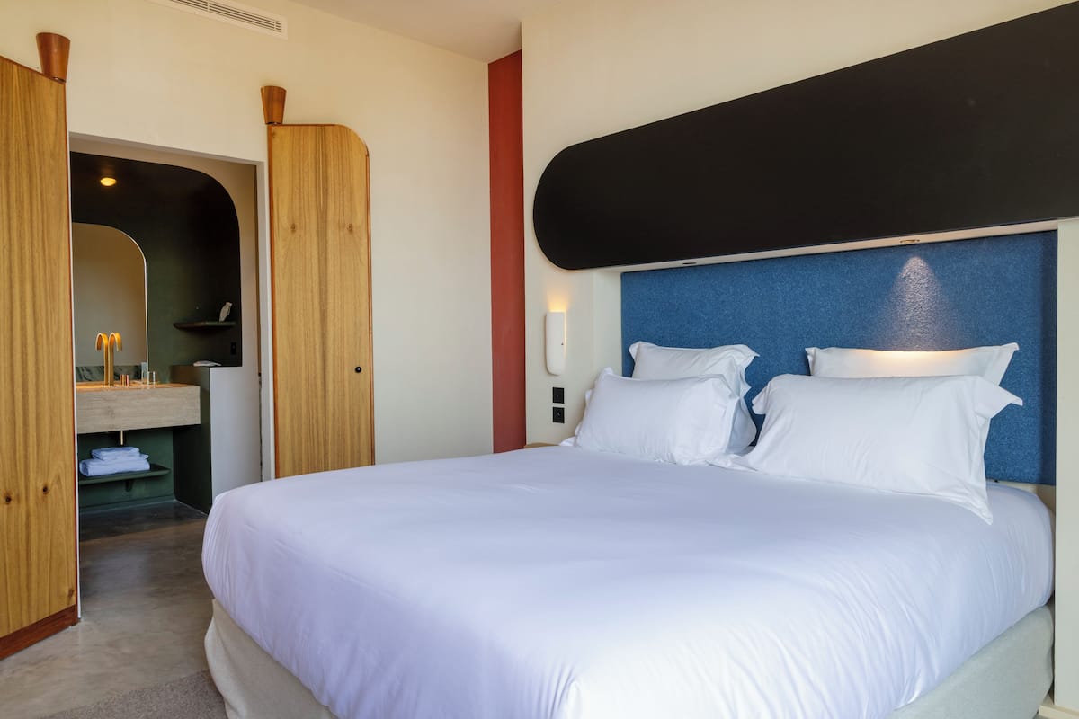 Ein Hotelzimmer mit einem großen Bett, einem Holzschrank, einem Spiegel und einem kleinen Badebereich.