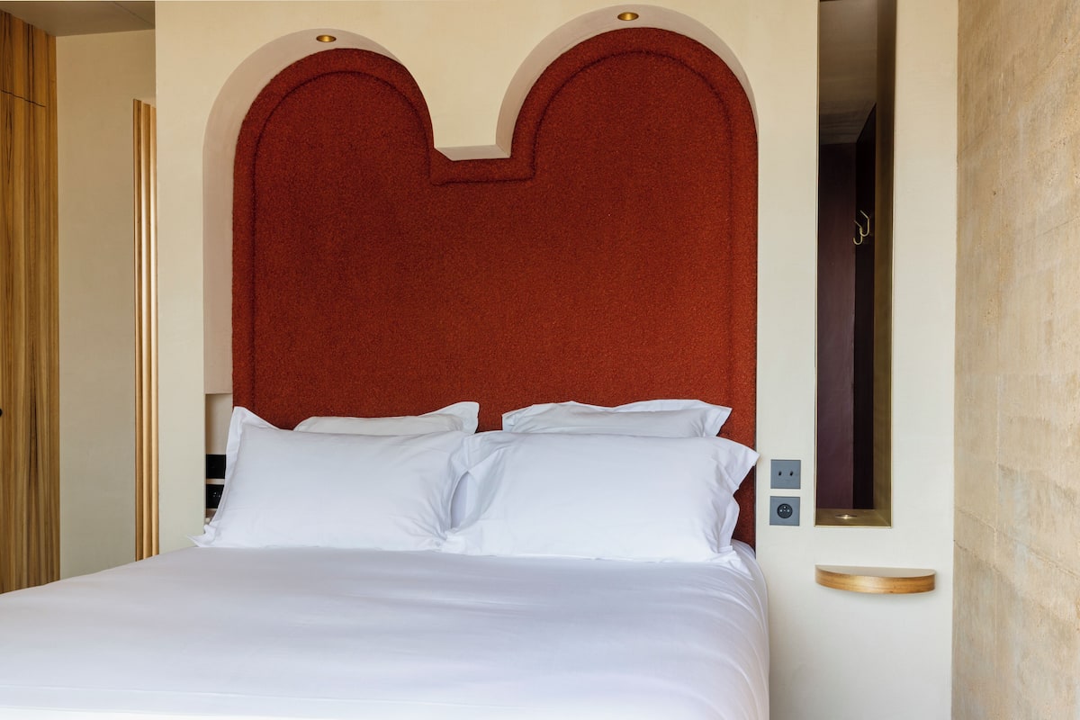 Ein Bett mit weißen Bettwäsche, einem roten Kopfteil und einem kleinen Nachttisch mit Spiegel.