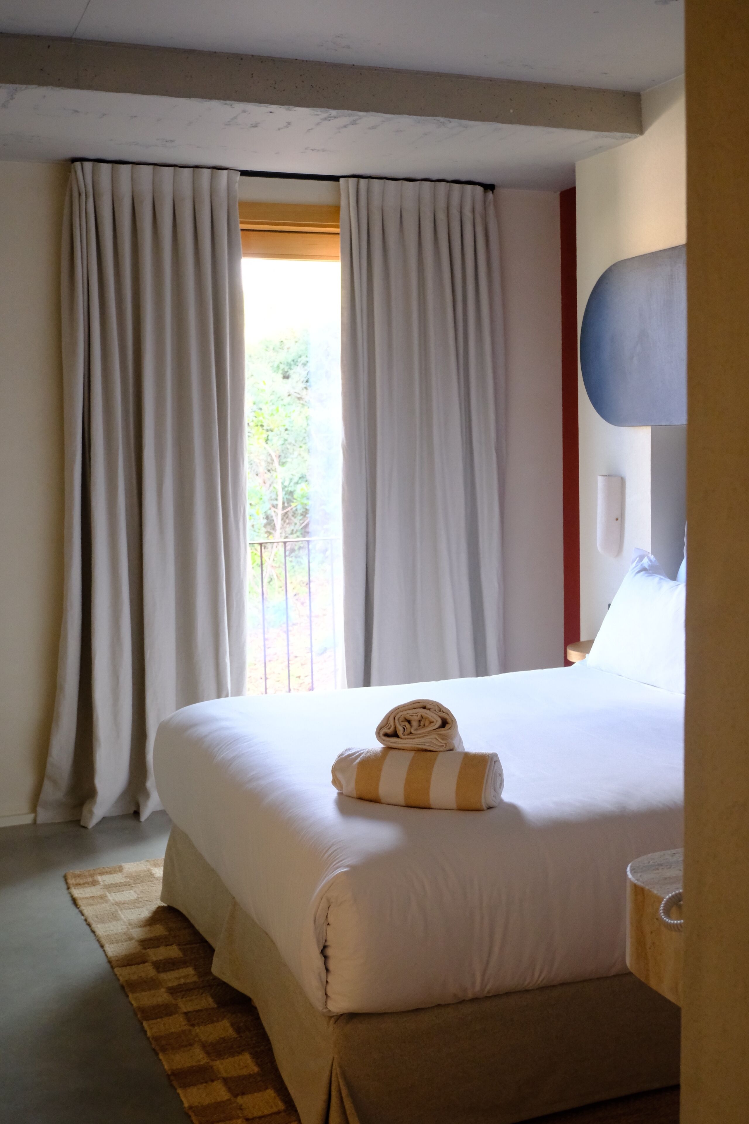 Quarto de hotel com uma cama grande, cortinas, vista para o verde lá fora e um tapete xadrez.