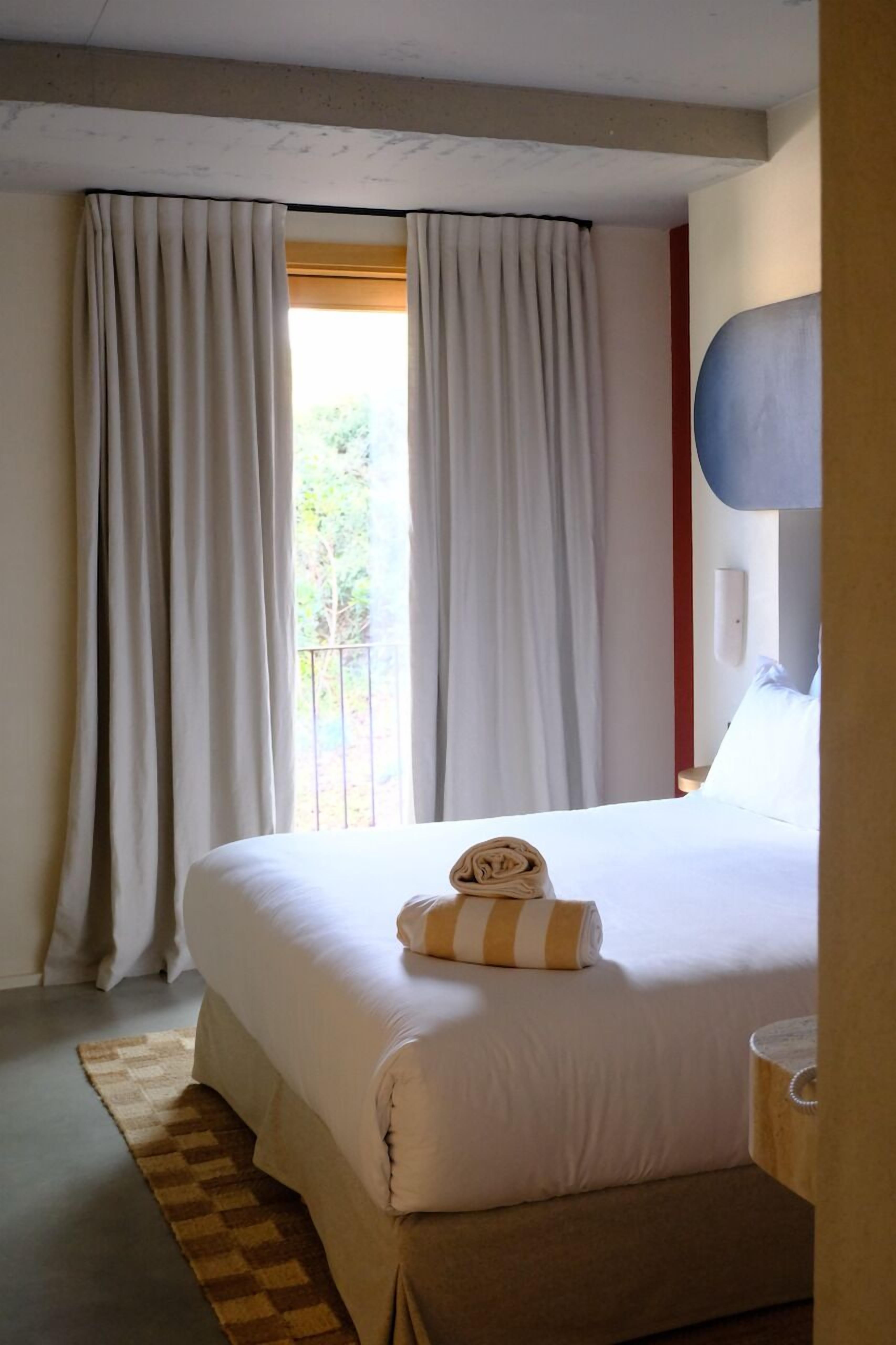 Habitación de hotel con una cama grande, cortinas blancas, vistas por la ventana y una alfombra a cuadros.