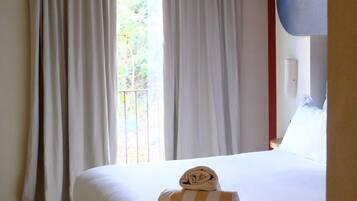Habitación de hotel con una cama grande, cortinas blancas, vistas por la ventana y una alfombra a cuadros.