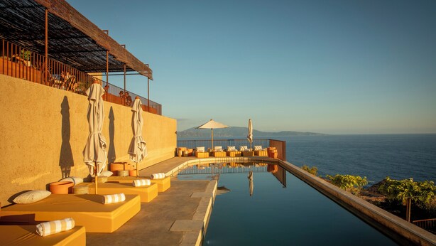 A poolside area with sun loungers and umbrellas, overlooking a body of water. -  Hôtel Mylos - Cargèse (Cargèse)