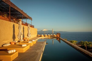 Zona junto a la piscina con tumbonas y sombrillas, con vistas a un cuerpo de agua.
