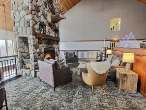 A stone fireplace with a mounted deer head, a lounge area with leather sofas, a wooden coffee table, and a stone wall. - Lutsen Ski-In/Ski-Out | Lake View | Pet-Friendly (Lutsen)