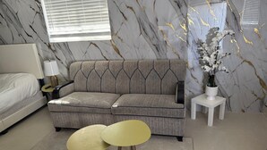 Ein modernes Schlafzimmer mit einem Bett, einem Schlafsofa, zwei kleinen Tischen und einer dekorativen Vase mit Blumen.