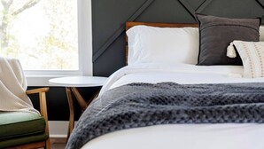 Ein ordentlich bezogenes Bett mit grauer Decke, einem Holzkopfschild und einem kleinen runden Tisch daneben.
