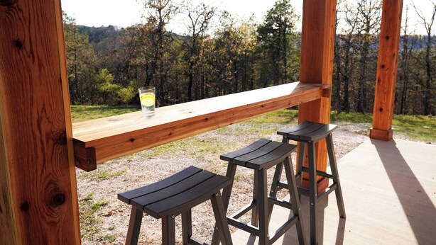Eine Holzterrasse mit einer Bank und zwei Hockern mit Blick auf ein bewaldetes Gebiet.