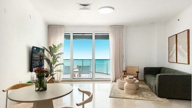 Un salon moderne comprenant un canapé, une table à manger avec des chaises, une table basse et une vue sur la mer grâce à de grandes fenêtres.